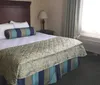 The image shows a neatly made bed with decorative pillows in a tidy hotel room with an air conditioning unit under the window