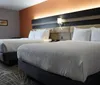 The image shows a modern hotel room with two neatly made double beds a warm lighting scheme and contemporary decor