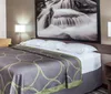 The image shows a neatly made bed with a unique green and purple patterned bedspread in a tidy hotel room with a large black and white nature photograph on the wall