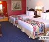 A warmly lit hotel room with a queen-size bed a decorative blanket framed artwork on the walls a small table with chairs and an entertainment unit displaying the logo Dutton Inn