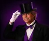 A person dressed in a formal magicians attire with a top hat bow tie and white gloves is smiling at the camera against a purple backdrop