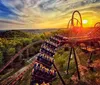 A roller coaster train ascends a track against a dramatic sunset sky offering a picturesque view of the surrounding landscape