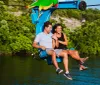 A man and a woman are smiling and enjoying a chairlift ride over a body of water surrounded by lush greenery