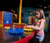 A young girl is engaged with an interactive exhibit involving colorful gears at a childrens museum