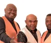 Three men in matching black and orange vests are posing together for a photo with one slightly in front of the other two all looking directly at the camera
