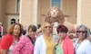 A group of five women is posing for a photo in front of a large lion statue outside a building with arched windows.