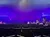 The image shows an indoor theater with an audience beginning to take their seats and a lit stage with purple lighting, hinting at an anticipation for a performance to begin.