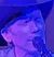 A person wearing a cowboy hat is playing an acoustic guitar and singing into a microphone on a stage with dim blue lighting.