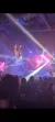 A performer is suspended mid-air during an aerial acrobatic act at a live event with colorful stage lighting and an audience in the foreground.