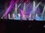 Performers on stage are singing and dancing in a brightly lit concert with a captivated audience.