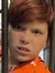 A child in an orange shirt with a dog print poses behind a fake jail cell in what appears to be a museum exhibit area.