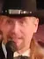 A person dressed as a wild west sheriff is speaking into a microphone on a stage with a rustic backdrop, as an audience eats and watches the performance.