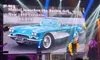 A presenter is speaking on stage with a backdrop featuring a 1959 Corvette and text about the launch of the Barbie doll, illuminated by stage lights and accompanied by musicians.
