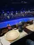 The image shows a dining area set with plates and drinks, overlooking an indoor arena with a large audience seated in preparation for an event or performance.
