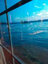 The image shows a serene view of a body of water and a small island seen through a window with some visible reflections and glare.