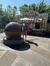 A man stands beside a large spherical fountain near an ice cream concession stand on a sunny day.