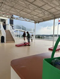 People are enjoying a leisurely game of cornhole on the deck of a boat with a scenic lake backdrop.