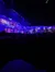 The image shows an audience watching a projection-mapped show or performance, featuring vibrant blue lighting and intricate architectural imagery.