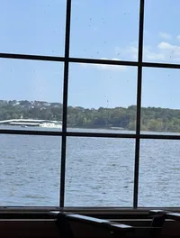 A clear day's view through a window pane with spots and streaks, overlooking a body of water with trees and buildings in the distance.
