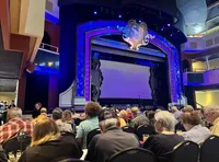 The image shows an elegantly decorated theater with an audience waiting in anticipation for a performance to begin.