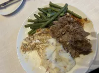 The image depicts a plate containing a serving of green beans, mashed potatoes, and shredded meat, possibly roasted or braised, with some gravy or sauce.