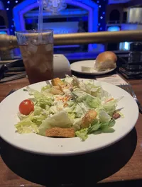 A plate of salad with a glass of iced tea is set on a table in front of a stage with blue lighting.