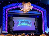 The image shows a brightly lit stage with ornate decorations and the words