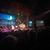 A band performs on stage in front of a captivated audience with a serene nighttime mountainous backdrop displayed on a screen behind them.
