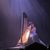 A musician is silhouetted by a beam of light as they play the harp on stage in front of an audience.