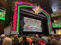 An audience is seated at tables in a decorative venue waiting for a performance to start, as indicated by the large, ornate