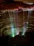 The image shows a cave with delicate waterfalls illuminated by colorful lights.