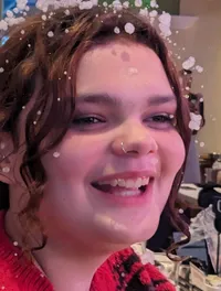 A person wearing a red festive sweater smiles while surrounded by artificial snow in a restaurant setting.