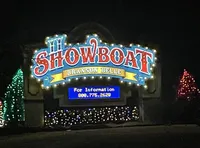 The image shows a brightly lit sign for the Showboat Branson Belle, surrounded by colorful lights and decorated trees.