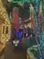 A festive street scene is illuminated with vibrant Christmas lights as people stroll along pathways decorated with colorful displays.