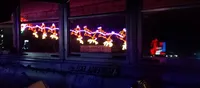 The image shows a window view with colorful, festive lights in the shape of reindeer and a sleigh, reflecting a Christmas scene.