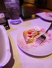 A partially eaten dessert with whipped cream and a fork sits on a plate beside a glass of water and a phone on a table.