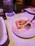 A partially eaten dessert with whipped cream and a fork sits on a plate beside a glass of water and a phone on a table.