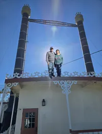A couple is standing on the edge of a decorative building with tall smokestacks under a clear blue sky.