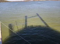 A shadow of a dock or structure is cast onto a body of water, with distant hills and calm waters in the background.