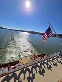 The image shows a sunny day over a body of water viewed from a boat with an American flag, leaving a trail in the water.