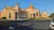 The image shows a large, elegant building with multiple domes and arched windows, set against a clear blue sky.