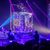 A performer is hanging upside down inside a metal frame on a stage with dramatic purple and blue lighting.
