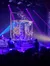A performer is hanging upside down inside a metal frame on a stage with dramatic purple and blue lighting.