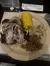 A plate of food featuring a half chicken, a piece of corn on the cob, diced potatoes, and pulled pork.