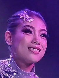 A performer is balancing on a tall stack of chairs set against a vibrant purple and blue stage backdrop.