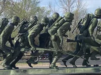 The image depicts a bronze statue of soldiers in combat gear, marching forward with weapons and backpacks.