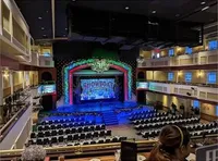 The image shows an empty theater with elaborate decorations and a stage set up for a show titled
