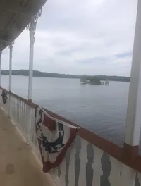 The image shows a view of a lake with a small island in the distance, seen from a boat deck adorned with a decorative red, white, and blue banner.