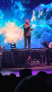 A person is performing on stage with vibrant, cosmic visuals in the background.