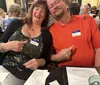 A smiling man and woman sitting together at a table, each wearing name tags and pointing playfully at each other.